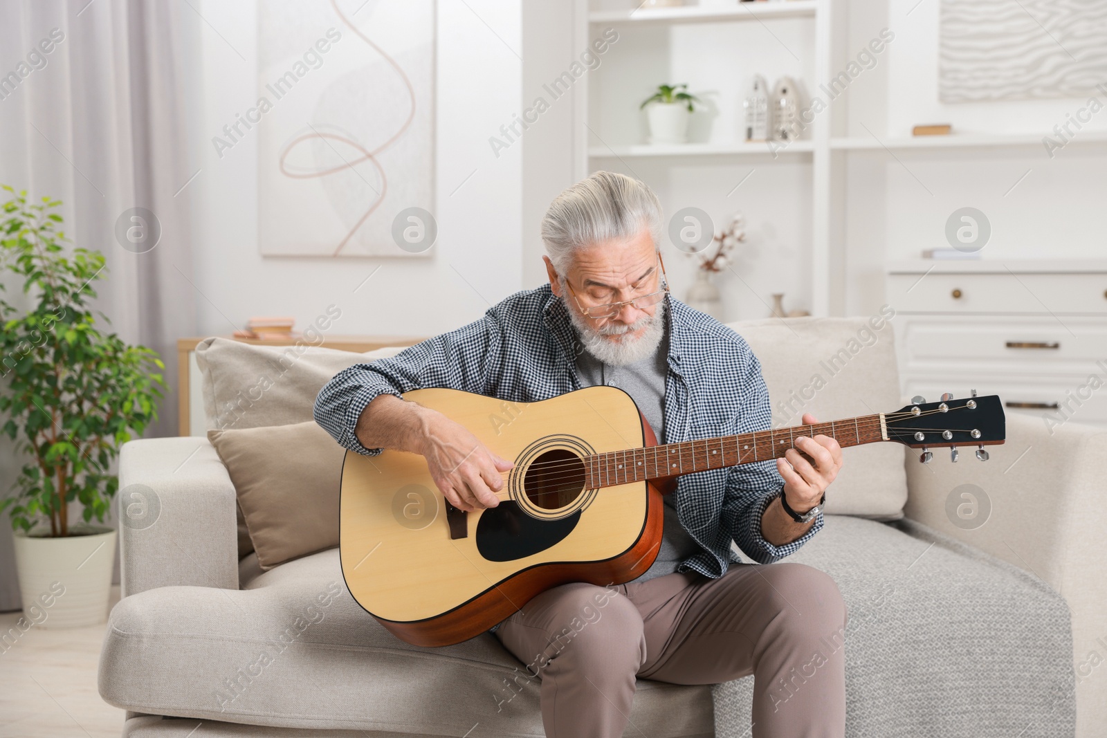 Photo of Relaxing hobby. Senior man playing guitar on sofa at home