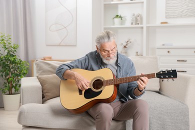 Photo of Relaxing hobby. Senior man playing guitar on sofa at home