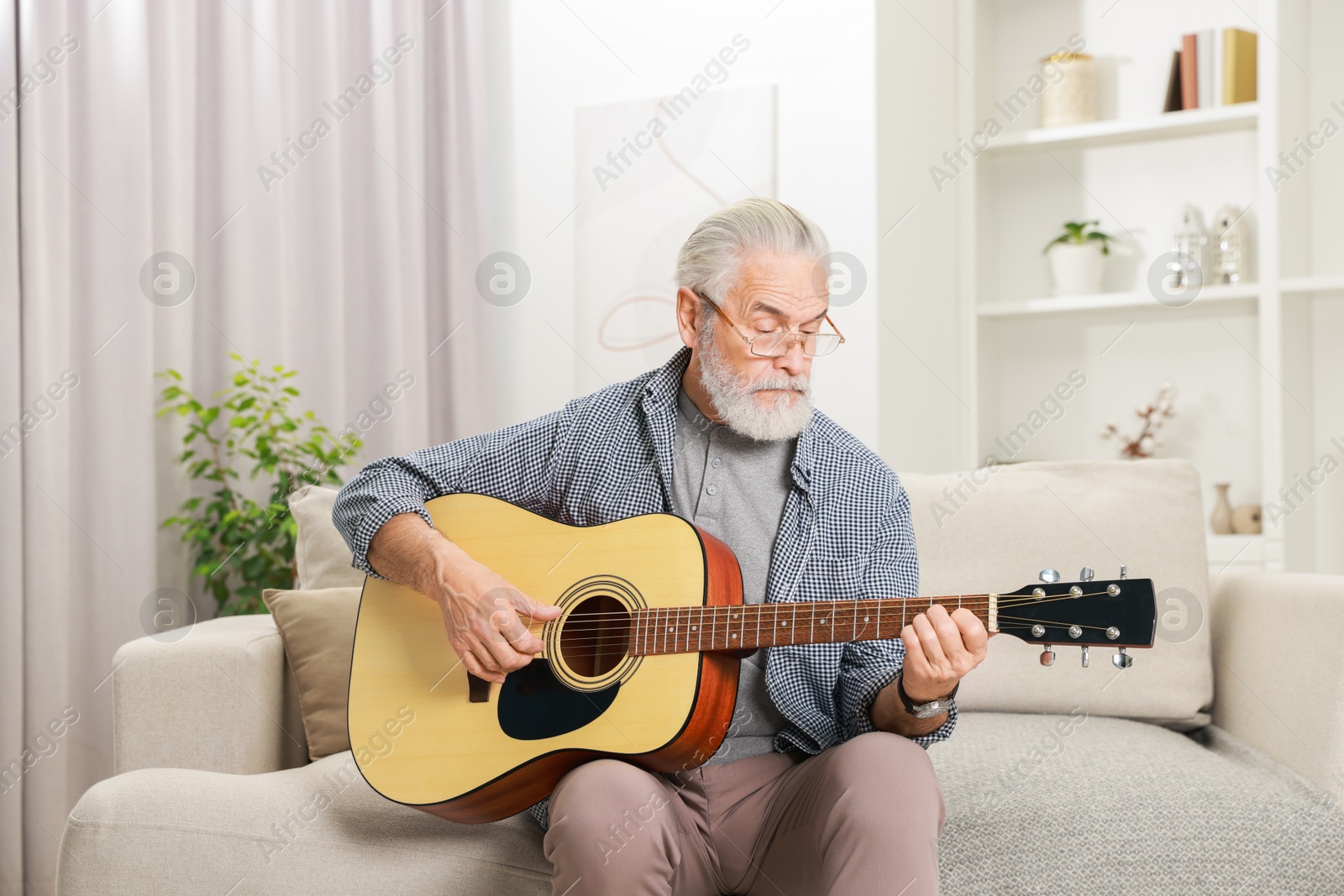 Photo of Relaxing hobby. Senior man playing guitar on sofa at home