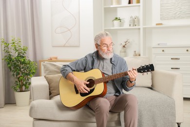 Photo of Relaxing hobby. Senior man playing guitar on sofa at home