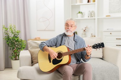 Photo of Relaxing hobby. Senior man playing guitar on sofa at home