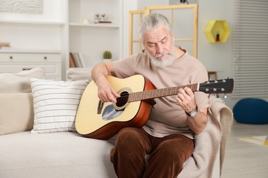 Photo of Relaxing hobby. Senior man playing guitar on sofa at home