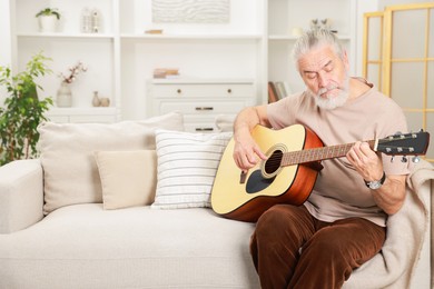 Photo of Relaxing hobby. Senior man playing guitar on sofa at home