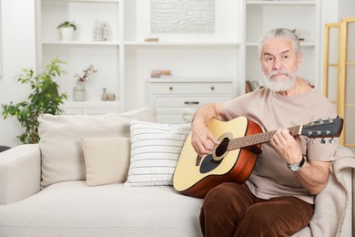 Photo of Relaxing hobby. Senior man playing guitar on sofa at home