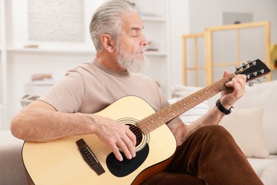 Photo of Relaxing hobby. Senior man playing guitar on sofa at home