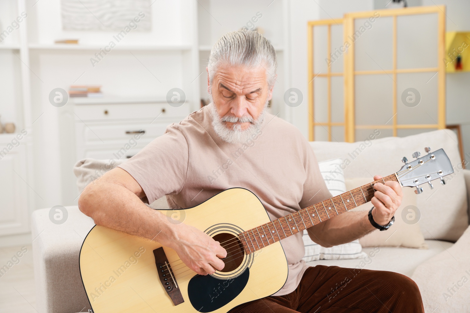 Photo of Relaxing hobby. Senior man playing guitar on sofa at home