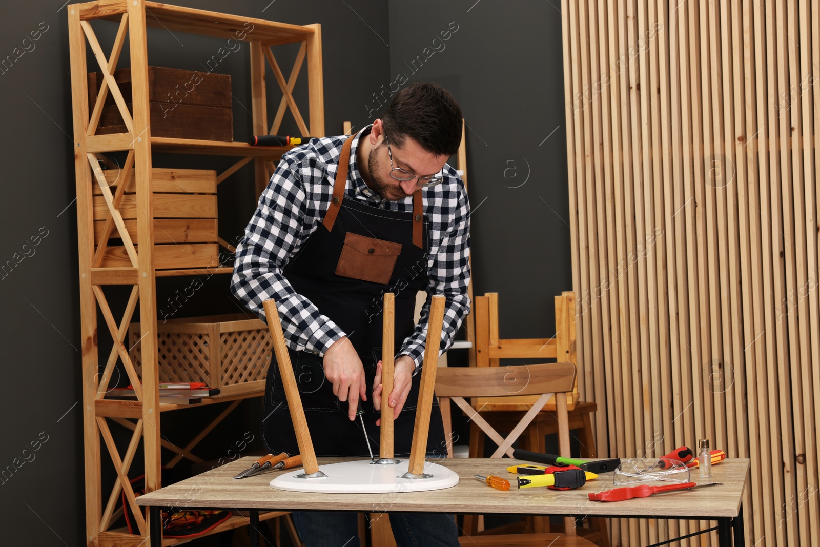 Photo of Relaxing hobby. Man assembling stool with screwdriver at table in workshop