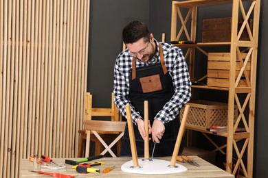 Photo of Relaxing hobby. Man assembling stool with screwdriver at table in workshop