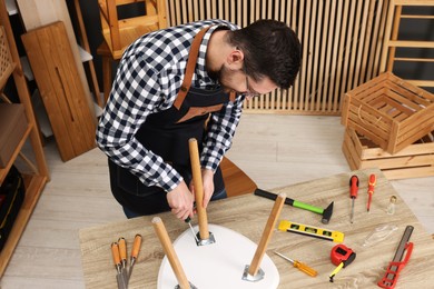 Photo of Relaxing hobby. Man assembling stool with screwdriver at table in workshop