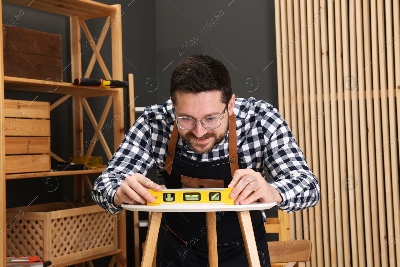 Photo of Relaxing hobby. Man using level tool while repairing stool in workshop