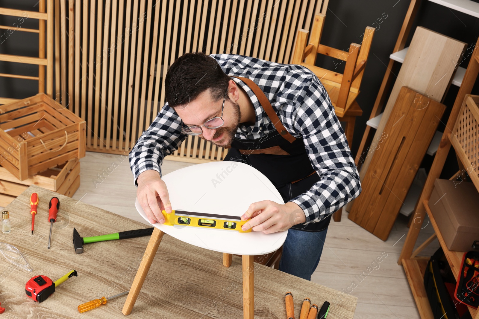 Photo of Relaxing hobby. Man using level tool while repairing stool at wooden table in workshop