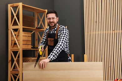 Photo of Relaxing hobby. Smiling man sawing wooden plank at table in workshop