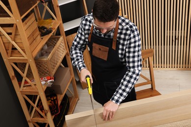 Photo of Relaxing hobby. Man sawing wooden plank at table in workshop