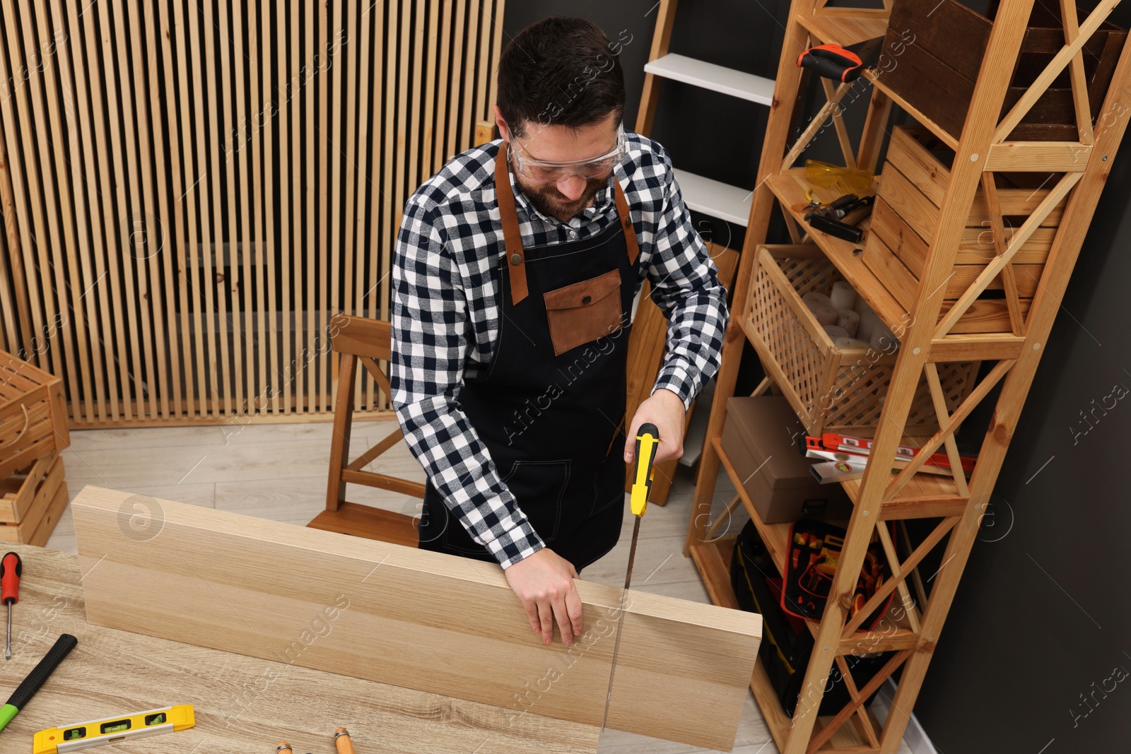 Photo of Relaxing hobby. Man sawing wooden plank at table in workshop