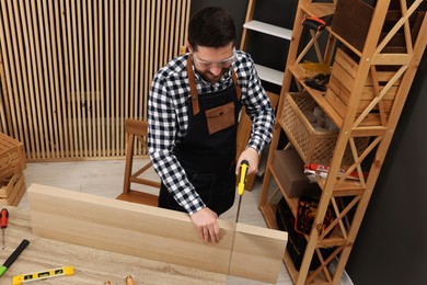 Photo of Relaxing hobby. Man sawing wooden plank at table in workshop