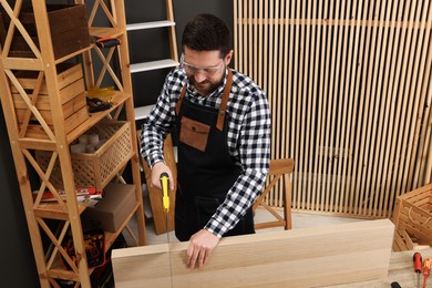 Photo of Relaxing hobby. Man sawing wooden plank at table in workshop