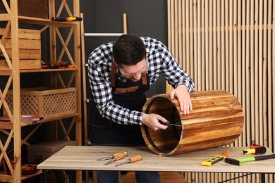 Photo of Relaxing hobby. Man assembling wooden trash can with screwdriver at table in workshop