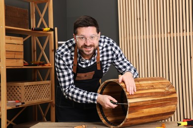 Photo of Relaxing hobby. Smiling man assembling wooden trash can with screwdriver at table in workshop