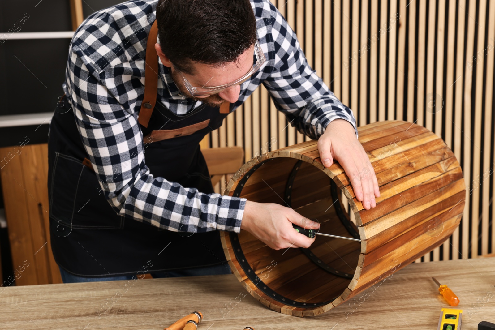 Photo of Relaxing hobby. Man assembling wooden trash can with screwdriver at table in workshop