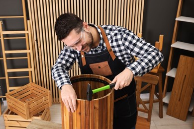 Photo of Relaxing hobby. Man repairing wooden trash can with hammer in workshop