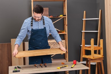 Photo of Relaxing hobby. Man with wooden plank at table in workshop