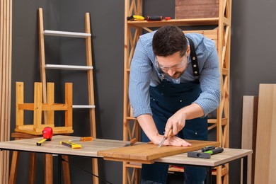 Photo of Relaxing hobby. Man working with wooden plank and chisel at table in workshop