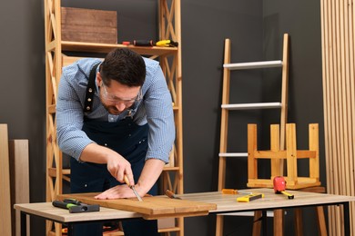 Photo of Relaxing hobby. Man working with wooden plank and chisel at table in workshop