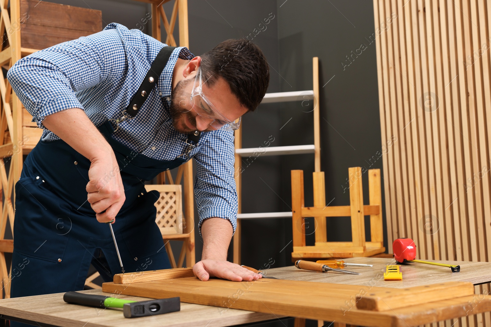 Photo of Relaxing hobby. Man working with wooden plank and screwdriver at table in workshop