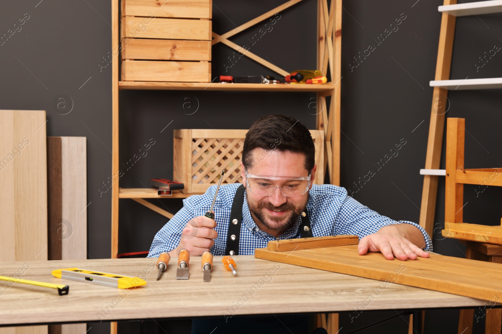 Photo of Relaxing hobby. Happy man with wooden plank and carpentry tools at table in workshop