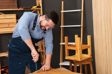 Photo of Relaxing hobby. Man working with wooden plank and screwdriver at table in workshop