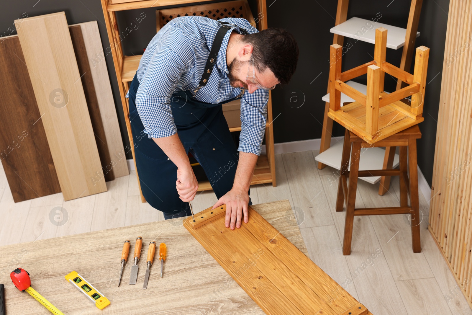 Photo of Relaxing hobby. Man working with wooden plank and screwdriver at table in workshop, above view