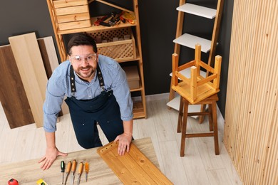 Photo of Relaxing hobby. Smiling man with wooden plank and carpentry tools at table in workshop, above view