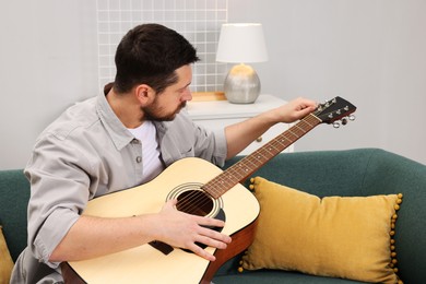 Photo of Relaxing hobby. Man playing guitar on sofa at home