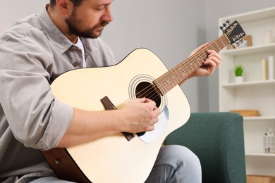 Photo of Relaxing hobby. Man playing guitar on sofa at home, closeup