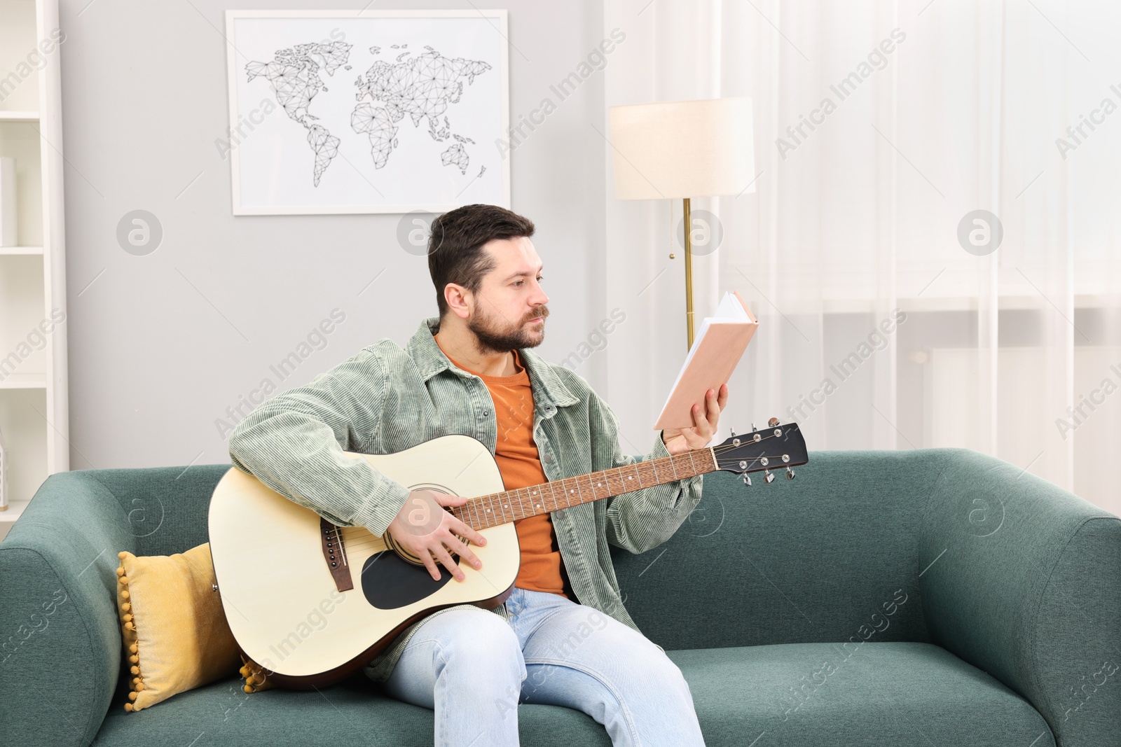 Photo of Relaxing hobby. Man with guitar and book on sofa at home