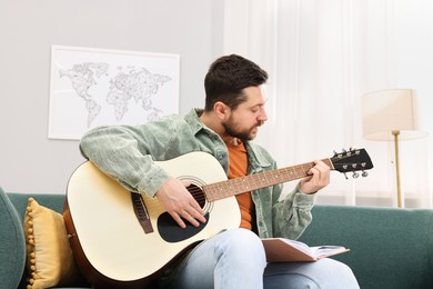 Photo of Relaxing hobby. Man with guitar and book on sofa at home