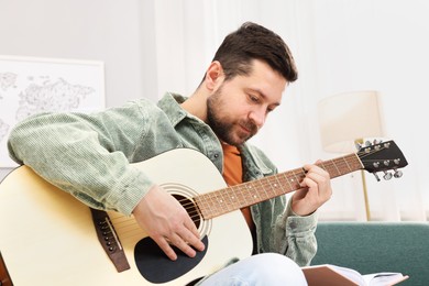 Photo of Relaxing hobby. Man with guitar and book at home