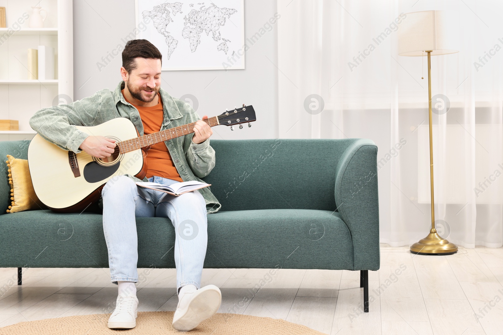 Photo of Relaxing hobby. Man with guitar and book on sofa at home