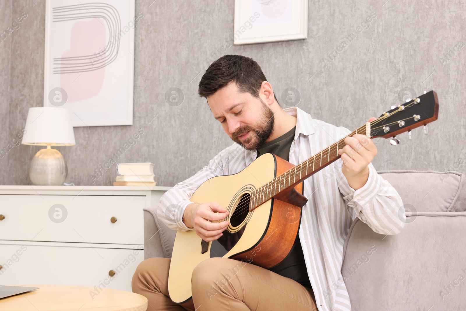 Photo of Relaxing hobby. Man playing guitar on armchair at home