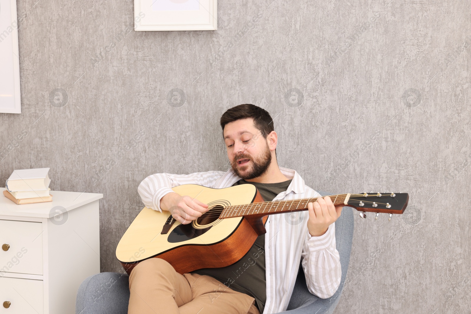 Photo of Relaxing hobby. Man playing guitar and singing on armchair at home