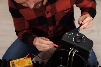 Photo of Relaxing hobby. Man testing deep fryer with multimeter indoors, closeup