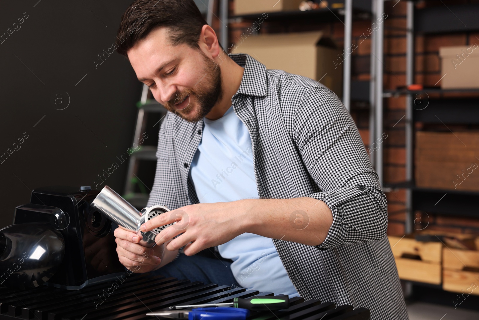 Photo of Relaxing hobby. Man examining parts of electric meat grinder in workshop