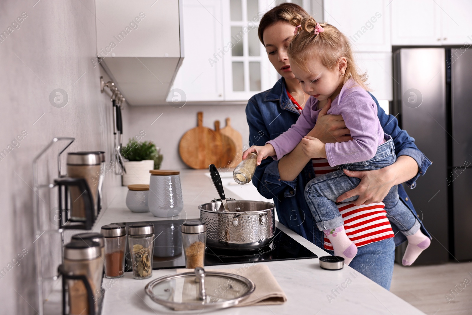 Photo of Busy housewife cooking with her little daughter in kitchen