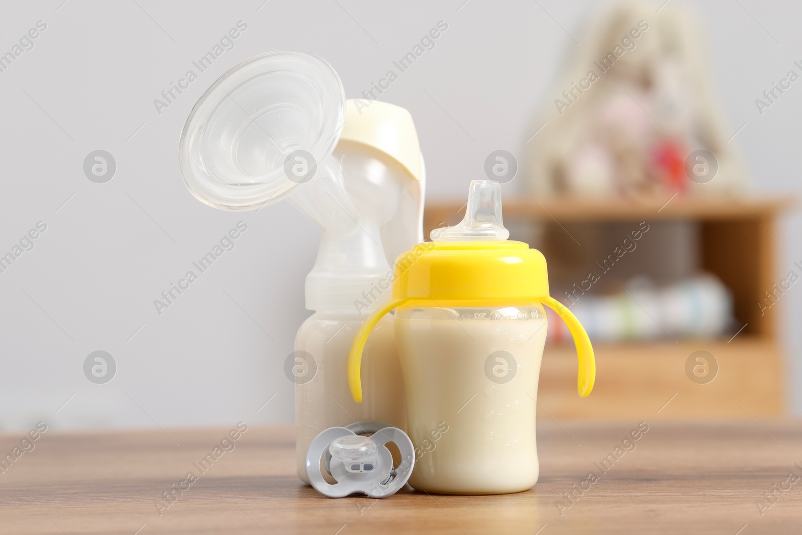 Photo of Feeding bottles with milk, breast pump and pacifier on wooden table indoors