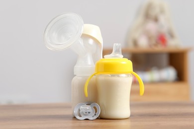 Photo of Feeding bottles with milk, breast pump and pacifier on wooden table indoors