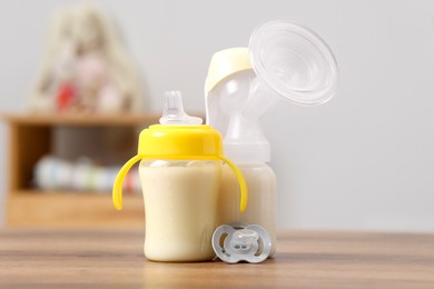 Photo of Feeding bottles with milk, breast pump and pacifier on wooden table indoors