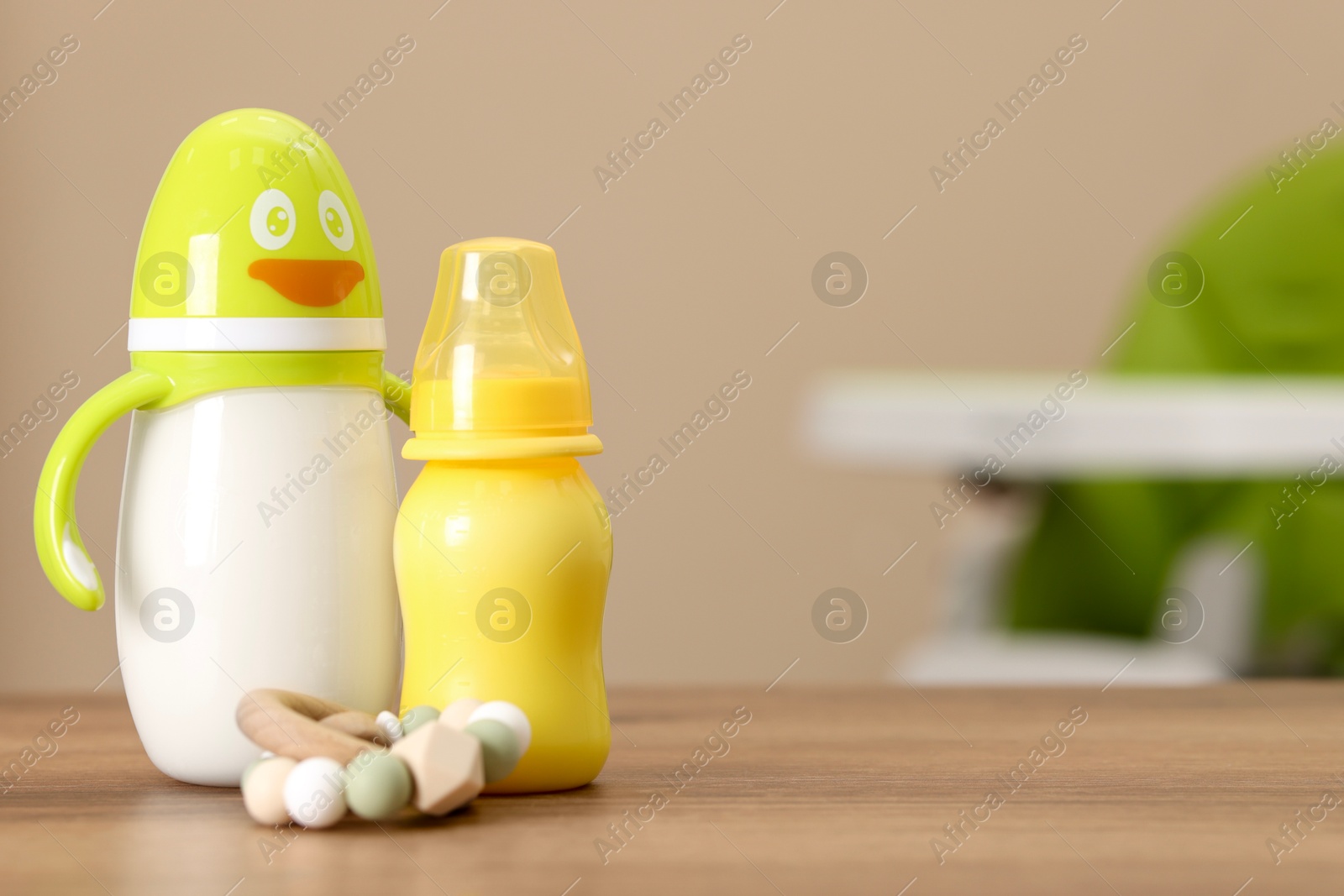 Photo of Feeding bottles with milk and toy on wooden table indoors, space for text