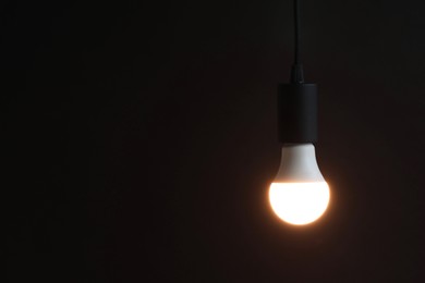 Photo of Glowing light bulb hanging on dark background. Space for text