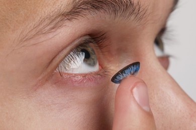 Photo of Man putting color contact lens in his eye, closeup