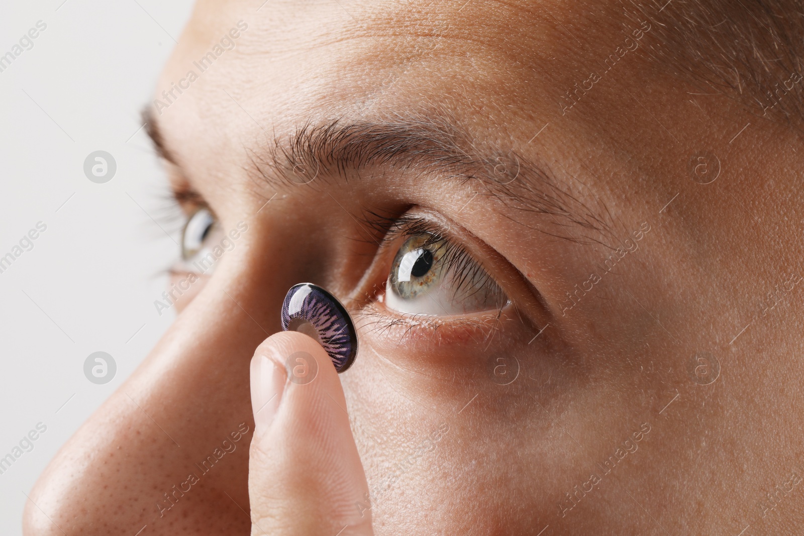 Photo of Man putting color contact lens in his eye on light background, closeup